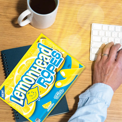 Lemon Candy Ropes Soft And Chewy With Tart Citrusy Lemon Flavor Bright Yellow Treat Packed With Dope Zest box on a desk with notebook and coffee