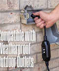 Hand plugging the electric pressure washer into a weatherproof outdoor outlet on brick wall.