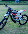 Adult Electric Dirt Bike Built To Shred With Raw Torque And 53 MPH Top Speed displayed on grass with knobby tires and sturdy chassis.