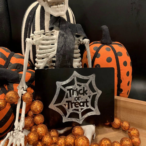Skeleton decor holding Trick or Treat blank anodized aluminum engraving sheet with pumpkins and orange glitter balls
