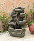 Six Tier Cascading Rock Outdoor Water Fountain With Lights For Garden Patio Backyard Deck And Porch No Fuss Setup With Pump 24.4 Inch High 110V Plug standing on a patio with a basketball beside it.