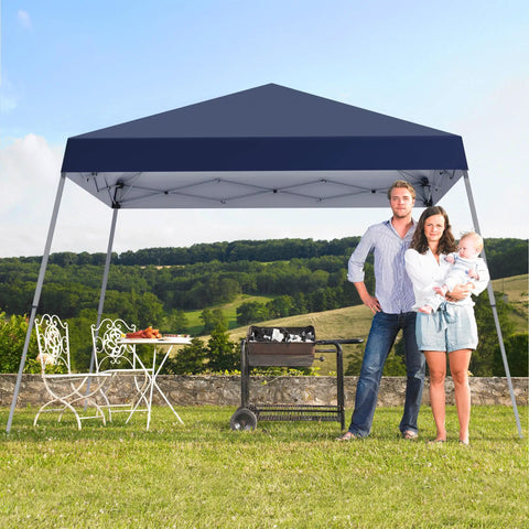 Dark blue fast pop up canopy tent 10x10 ft with slant legs set up on grass with family, table, and grill nearby