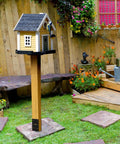 Backyard scene with a wooden post and birdhouse, secured on a Heavy Duty U Shaped Fence Post Anchor Ground Spike 4 x 4 In Concrete Base.