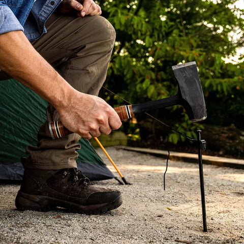 Top Shelf 14 Inch Wood Splitting Maul With Forged Steel Head And Kickless Grip being used to hammer a tent stake at a campsite.