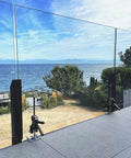 Viking Arm handheld jack/clamps installed on glass railing posts along an outdoor deck overlooking the sea.