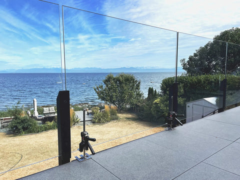 Viking Arm handheld jack/clamps installed on glass railing posts along an outdoor deck overlooking the sea.