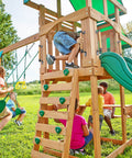Children playing on a wooden playset with swings and slide in a grassy yard