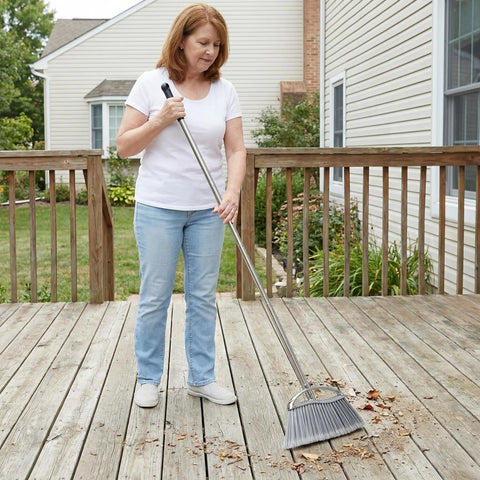 Heavy Duty Angle Broom Featuring Rigid Bristles And An Extended Handle That Smashes Through Stubborn Dirt And Leaves On Patios Garages And Commercial Floors Like Butter being used to clean leaves on a wooden deck.