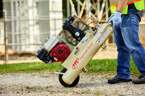 Person carrying 135 Psi 5.5 Hp Gas Powered Air Compressor with Honda engine and wheelbarrow design on gravel.