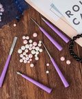 Front view of Mudder bead reamer set with 10 purple-handled, diamond-tipped tools beside pink and white beads on a wooden surface