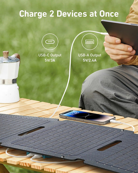 Solix PS30 Foldable 30W Solar Panel Charger charging devices outdoors on a wooden table, demonstrating dual USB-A and USB-C ports.