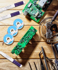 Soldering Pen And Solder Wick Kit For Electronics Repair with 3 pens and 3 wick strips shown on a wooden table.