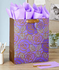 Large Purple Floral Gift Bag With Gold Foil Accents, Satin Ribbon Handles, And Purple Tissue Paper, 13 Inch Tall on desk