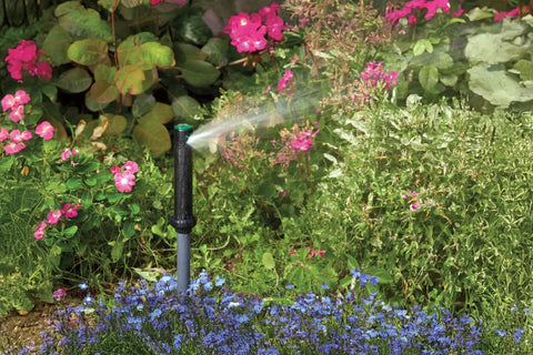 Gear Drive Rotor Shrub Sprinkler With Adjustable Arc Range And 25 Foot Reach spraying water among colorful flowers in a garden.