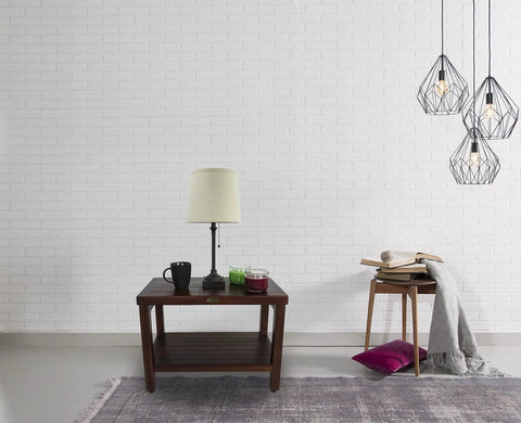 Living room with teak side table, lamp, books, and geometric pendant lights against a white brick wall.