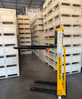 Self Loading Electric Pallet Stacker With 2116 Lbs Capacity And 51 Inch Lift Height in warehouse next to wooden pallets.