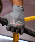 Close-up of a hand wearing grey knit wrist gloves holding a metal bar, showcasing 12 Pack Safety Performance Series Work Gloves For Construction And Mechanics Heavy Duty With Breathable Flex Superior Dexterity Knit Wrist Keeps Dirt Out Grey Size Large Durable Grip For Tools And Hand Protection.