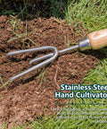 Stainless steel hand cultivator with wood handle used for loosening soil in garden; part of 3 Piece Garden Tool Set With Stainless Steel Hand Trowel Hand Cultivator And Hand Fork With Wood Handles Perfect For Weeding Transplanting Digging And Soil Loosening Soil And Composting Includes Durable Tools For Easy Garden Upkeep And A Great Gift.
