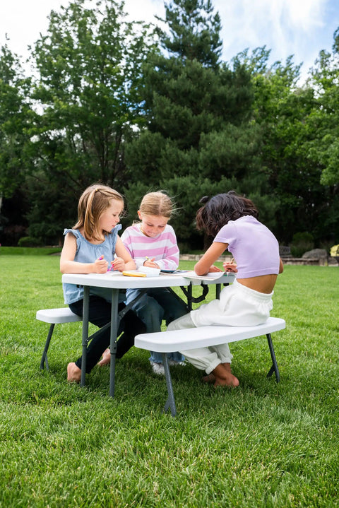 Three children drawing on a Compact Kids Picnic Table With Foldable Benches Under The Table And Built In Carry Handle For Easy Transport
