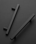 Two Matte Black 7-3/8 Inch Square Cabinet Pulls, Stainless Steel with 5 Inch Center-To-Center Holes, on a black surface