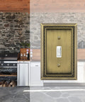 Sunken Pearls Beaded Wall Plate Switch Cover in antique brass shown against a rustic stone-walled kitchen setting.