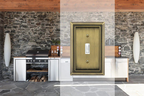 Sunken Pearls Beaded Wall Plate Switch Cover in antique brass shown against a rustic stone-walled kitchen setting.