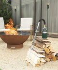 Self Igniting Outdoor Torch, 20,000 BTU High Output Flame, 36 Inch Handle leaning on wood near a fire pit
