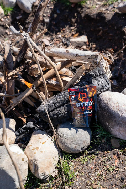 Pack of Fire Balls Fire Starter Pellets for Easy Fire Lighting, 7 Minute Burn Time, next to a campfire setting with rocks and logs.