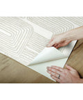 Hands peeling Nikki Chu Zulu Signature Peel And Stick Vinyl Wallpaper Roll for easy no mess install, wood surface shown.