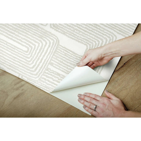 Hands peeling Nikki Chu Zulu Signature Peel And Stick Vinyl Wallpaper Roll for easy no mess install, wood surface shown.