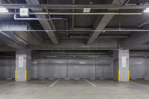 Interior of a modern parking garage featuring concrete walls, yellow pillars, and overhead piping.
