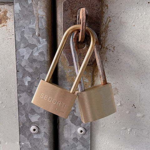 Two padlocks on a metal door hasp; brass SEDORTI 40mm lock and a copper-toned padlock.