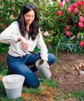 Woman using Spot Spreader 80 Oz Handheld Grab-And-Go Dispenser in garden with smart lid and strong handle among flowers