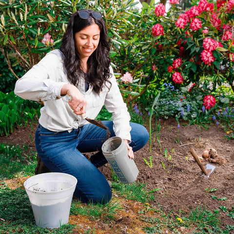 Woman using Spot Spreader 80 Oz Handheld Grab-And-Go Dispenser in garden with smart lid and strong handle among flowers