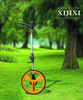 Foldaway Digital Distance Tracker Wheel With Illuminated Lcd Readout And Data Storage Built Ridiculously Tuff For Lawn And Job Site Use Roll Easy Outside Total Game Changer Includes Cozy Cloth Messenger Bag In Bright Yellow in grassy area with trees.