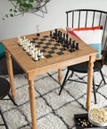 Wood table with chess setup beside chairs in cozy room, popcorn bowl on floor, emphasizing home leisure.