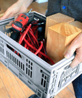Person carrying a Must-Have Collapsible Utility Crates Set Of 3 Grey 15.8L Stackable Folding Storage Bins filled with tools and wood.