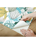 Teal And Yellow Retro Tropical Leaves Peel And Stick Wallpaper Roll For Accent Walls Dope Vibe being installed on wooden surface