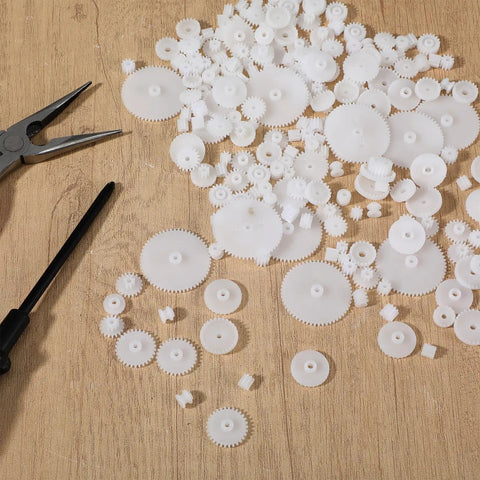 Assorted 200 Piece Plastic Gear Set Kit For DIYers Working On Models And Toys, spread on wood surface with tools visible.