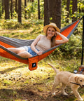 Person relaxing in Ultralight Camping Hammock For Hiking And Travel, Durable Outdoor Hammock In Orange, in a forest setting.
