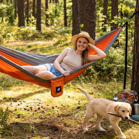 Person relaxing in Ultralight Camping Hammock For Hiking And Travel, Durable Outdoor Hammock In Orange, in a forest setting.