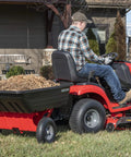 Tow Behind Poly Dump Cart With 10 Cu Ft Bed And 350 Lb Load Capacity attached to lawn tractor, transporting mulch.