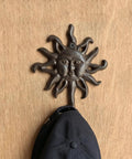 Heavy Duty Cast Iron Coat Hooks Set Of Two Vintage Sunburst Wall Mounts With Installation Screws Antique Dark Brown Rust Proof holding a cap.