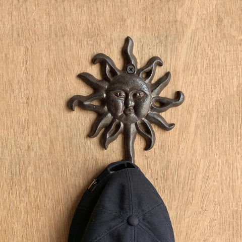 Heavy Duty Cast Iron Coat Hooks Set Of Two Vintage Sunburst Wall Mounts With Installation Screws Antique Dark Brown Rust Proof holding a cap.