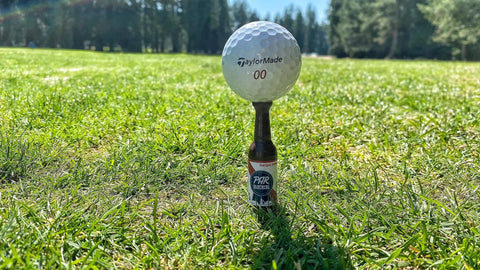 Beer Bottle Golf Tees Pack Of 6 For Golfers on a grass field holding a golf ball, virtually unbreakable recyclable plastic, 3-1/4 inches tall.