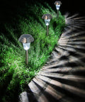Sweet 6 Pack Silver Solar Path Lights With Glass Lens And Metal Ground Stakes, illuminating a pathway with starburst glow