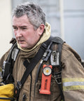 Firefighter with Survivor 175-Lumen Rechargeable Firefighter Right-Angle Flashlight attached to gear, rugged orange body visible.