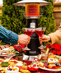 Portable Tabletop Propane Patio Heater With 11,000 BTU Power Adjustable Heat Safety Tilt Switch Burner Screen Guard Heats Up To 30 Sq Ft Black Outdoor Heater For Chill Nights on a dining table with food and drinks.