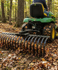 Cat-0 Agricultural Field Landscape Rake With Spring Steel Tines attached to tractor, clearing leaves in a wooded area