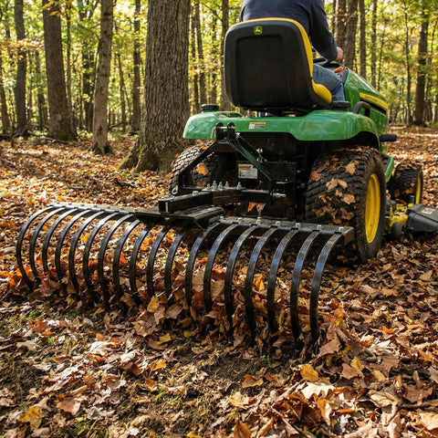 Cat-0 Agricultural Field Landscape Rake With Spring Steel Tines attached to tractor, clearing leaves in a wooded area